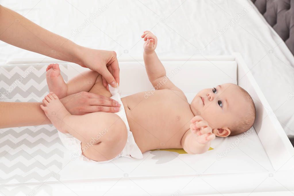 Mother changing her baby's diaper on table indoors