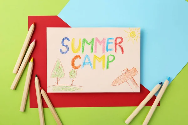 Papier mit schriftlichem Text Sommerlager, Zeichnungen und verschiedene Bleistifte auf farbigem Hintergrund, flache Lage — Stockfoto