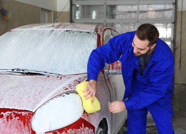 Worker cleaning automobile with sponge at professional car wash