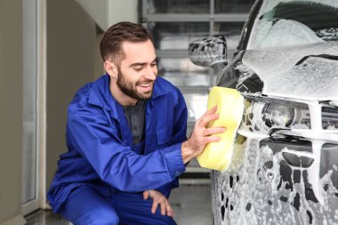 Worker cleaning automobile with sponge at professional car wash