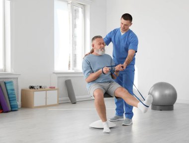 Professional physiotherapist working with senior patient in rehabilitation center clipart