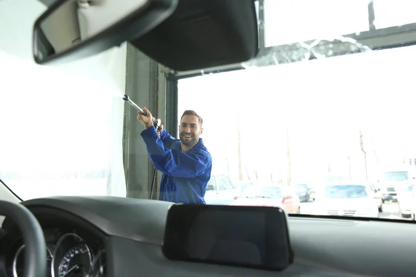 Worker cleaning automobile windshield with high pressure water jet at car wash, view from inside — 스톡 사진