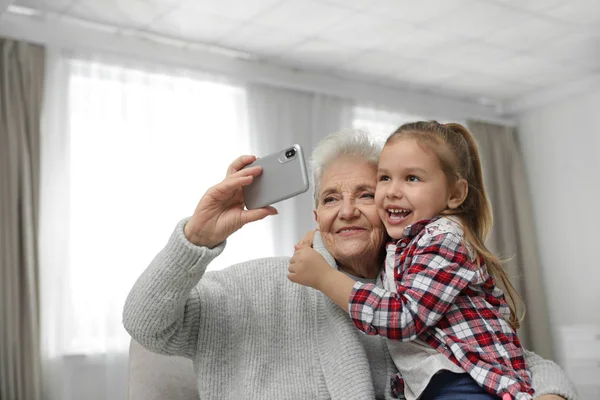 Menina bonito e sua avó tomando selfie em casa — Fotografia de Stock