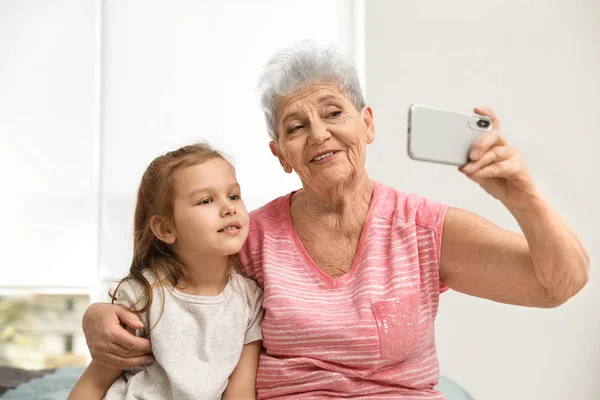 Menina bonito e sua avó tomando selfie em casa — Fotografia de Stock