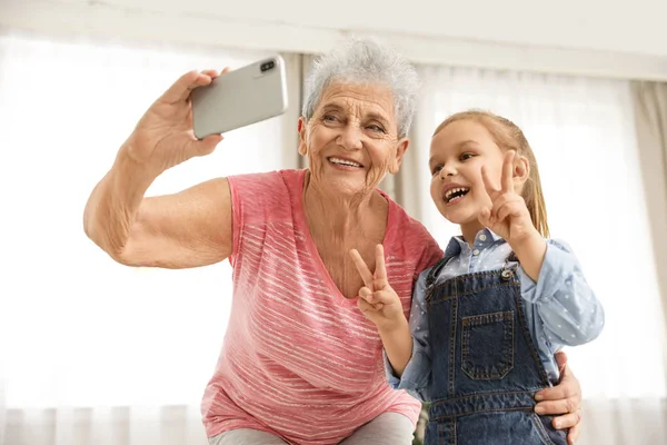 Menina bonito e sua avó tomando selfie em casa — Fotografia de Stock