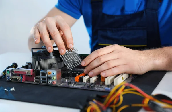 Male technician repairing motherboard at table, closeup