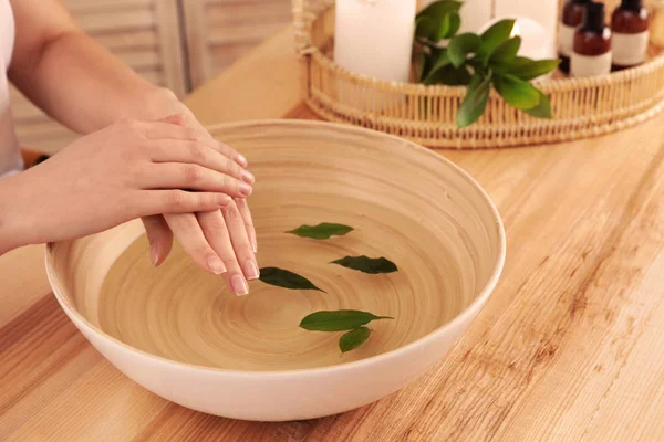 Femme trempant ses mains dans un bol d'eau et laisse sur une table en bois, en gros plan avec de l'espace pour le texte. Traitement spa — Photo