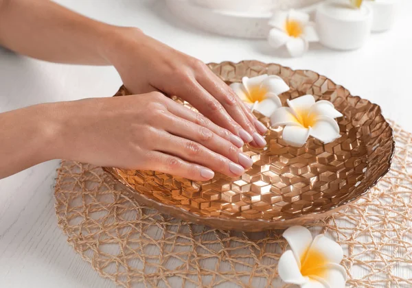 Mulher encharcando as mãos em tigela com água e flores na mesa, close-up. Tratamento de Spa — Fotografia de Stock