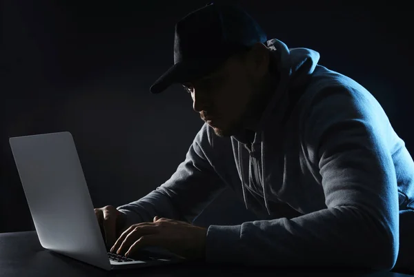 Hombre usando el ordenador portátil en la mesa sobre fondo oscuro. Actividad delictiva —  Fotos de Stock