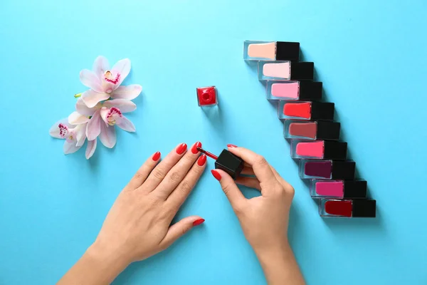 Mujer aplicando esmalte de uñas brillante sobre fondo de color, vista superior — Foto de Stock