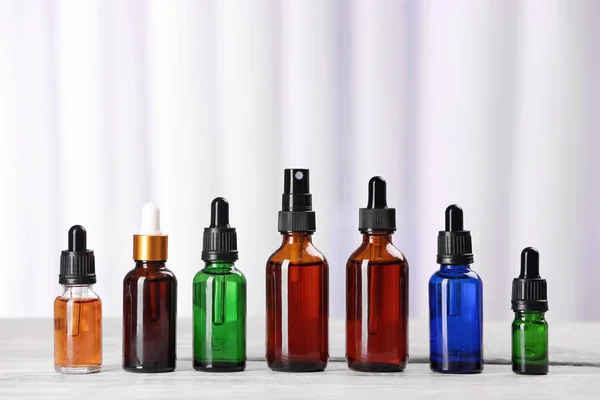 Flessen etherische oliën op tafel tegen lichte achtergrond. Cosmetische producten — Stockfoto