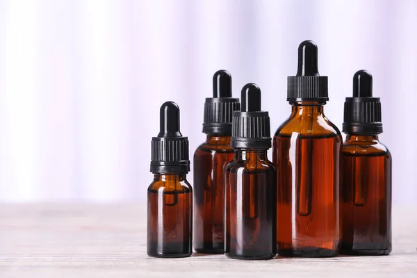 Flessen etherische oliën op tafel tegen lichte achtergrond, ruimte voor tekst. Cosmetische producten — Stockfoto