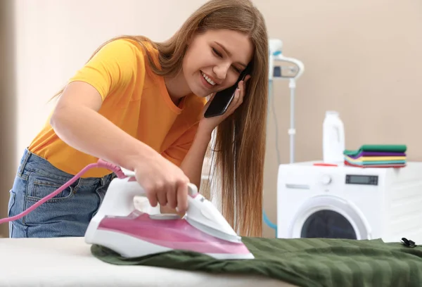 Glückliche Frau telefoniert, während sie im Badezimmer Wäsche bügelt. Raum für Text — Stockfoto