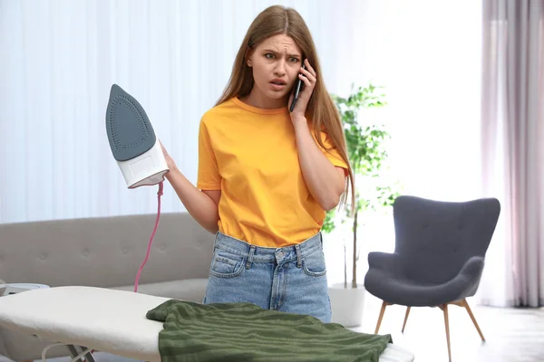 Эмоциональная женщина разговаривает по телефону во время глажки одежды дома — стоковое фото