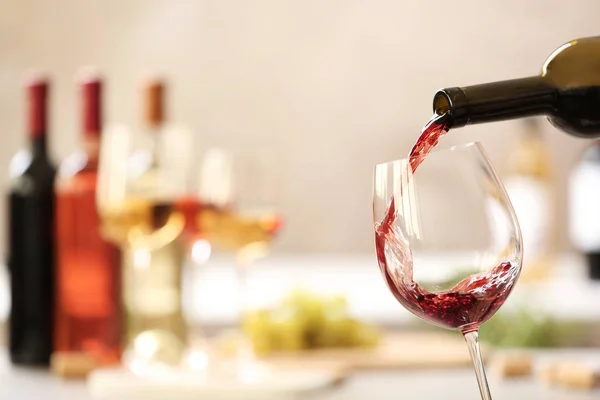 Выливание красного вина из бутылки в бокал на размытом фоне. Пространство для текста — стоковое фото