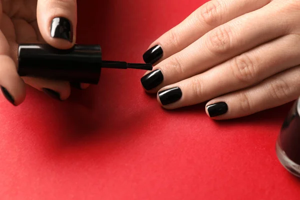 Vrouw toepassing van zwarte nagellak op kleur achtergrond, close-up — Stockfoto