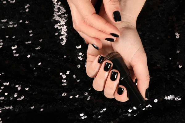 Woman with black manicure and nail polish bottle on dark background, top view. Space for text