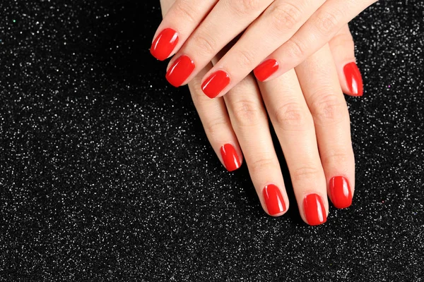 Жінка показує доглянуті руки з червоним лаком для нігтів на чорному тлі, вид зверху. Простір для тексту — стокове фото