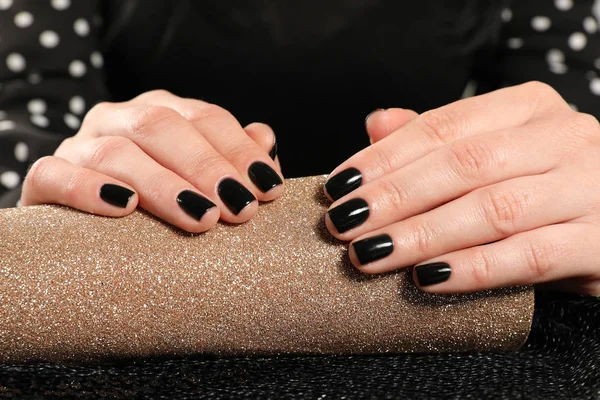 Vrouw met zwarte manicure op gerold glanzend papier, close-up. Nagellak trends — Stockfoto