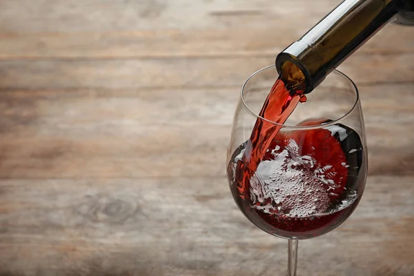 Pouring red wine from bottle into glass on wooden background. Space for text — Stock Photo, Image