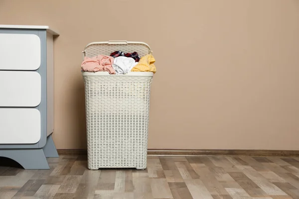 Plastic laundry basket with dirty clothes near color wall in room. Space for text