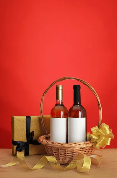 Бутылки вина в плетеной корзине с луком и подарок на столе на цветном фоне. Пространство для текста — стоковое фото