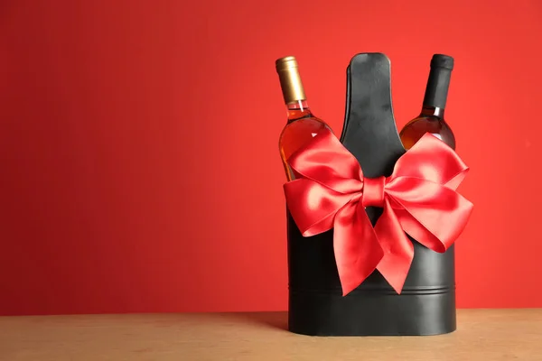 Bottles of wine in holder with bow on table against color background. Space for text