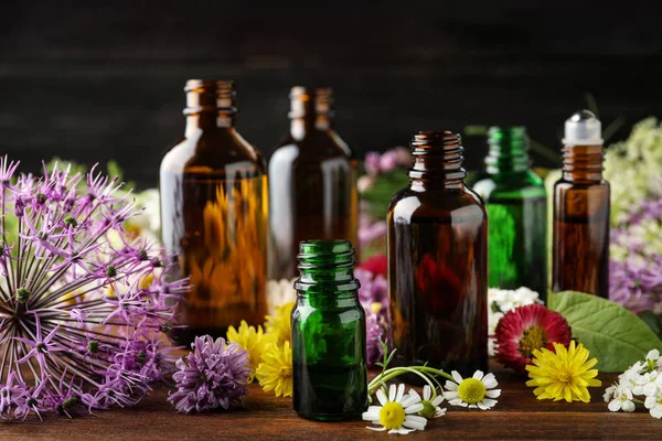 Diferentes botellas de aceites esenciales y flores en la mesa —  Fotos de Stock