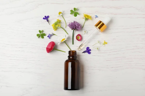 Botella de aceite esencial y diferentes flores sobre fondo de madera blanca, plano — Foto de Stock