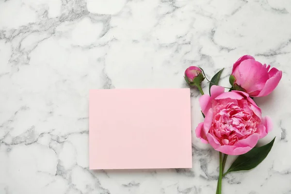 Peonías fragantes y tarjeta en blanco sobre mesa de mármol, vista superior con espacio para texto. Hermosas flores de primavera —  Fotos de Stock