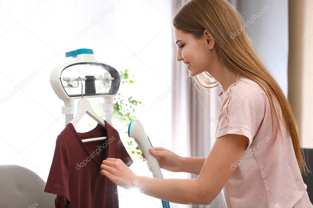 Young woman steaming her clothes on rack at home
