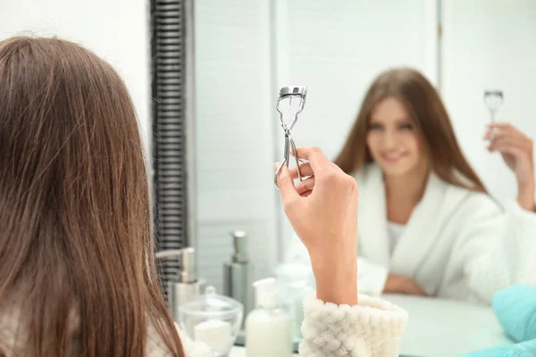 Молодая женщина с бигуди ресниц возле зеркала в ванной комнате, крупным планом — стоковое фото