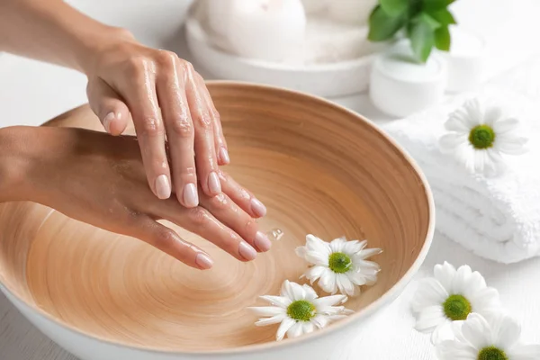 Vrouw doorweekt haar handen in een kom water en bloemen op tafel, close-up met ruimte voor tekst. Kuuroord — Stockfoto