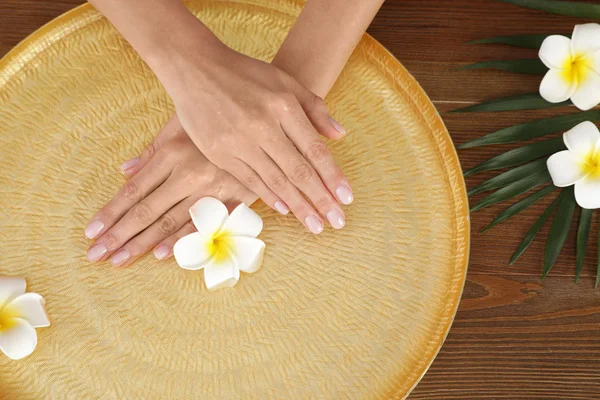 Femme trempant ses mains dans un bol avec de l'eau et des fleurs sur une table en bois, vue sur le dessus. Traitement spa — Photo