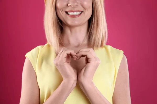 Vrouw maken van hart met haar handen op kleur achtergrond, close-up — Stockfoto