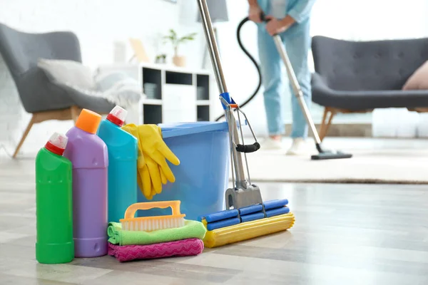 Detergents, bucket and mop on floor with janitor vacuuming carpet indoors — Stock Photo, Image