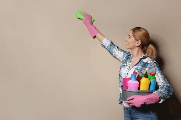 Mujer con lavabo de detergentes limpiando la pared de color. Espacio para texto — Foto de Stock