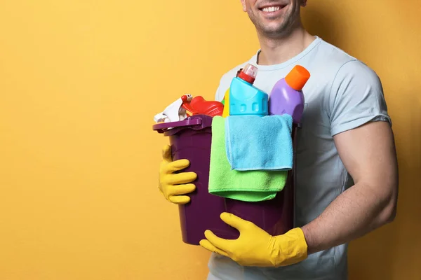Man met emmer detergenten op kleur achtergrond, close-up. Ruimte voor tekst — Stockfoto