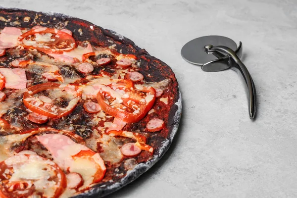 Black pizza and knife on grey table, closeup. Space for text