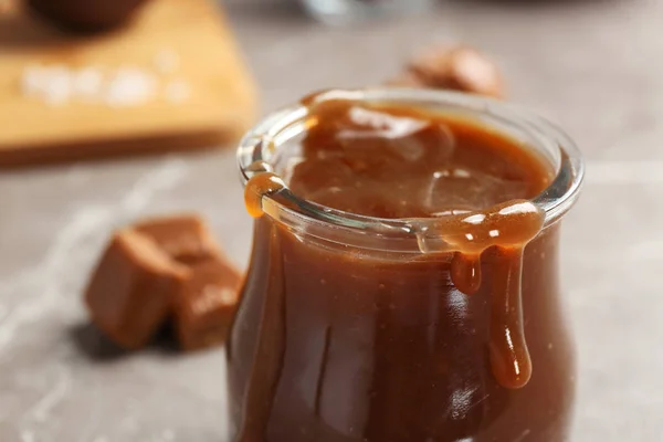 Borcan cu sos caramel gustos pe masă, closeup — Fotografie, imagine de stoc