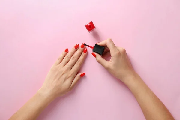 Mujer aplicando esmalte de uñas brillante sobre fondo de color, vista superior — Foto de Stock