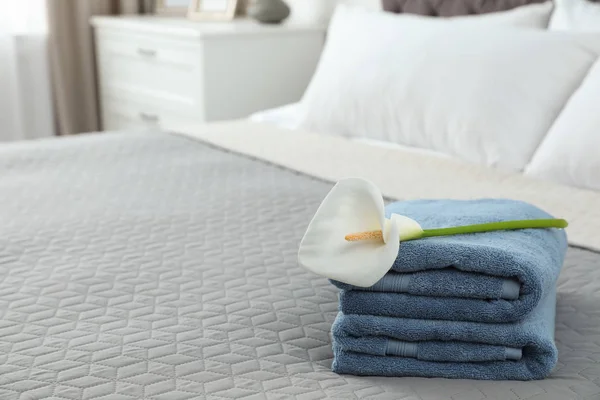 Стопка чистых полотенец с цветком на кровати в помещении. Пространство для текста — стоковое фото