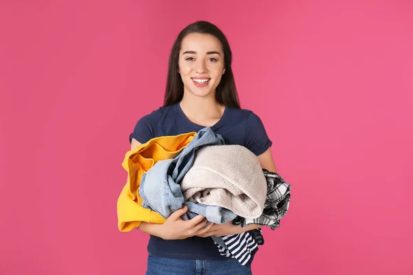 Happy young woman holding pile of dirty laundry on color background — Stock Photo, Image