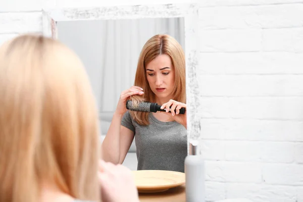 Emotional woman brushing hair near mirror in bathroom — Stock Photo, Image