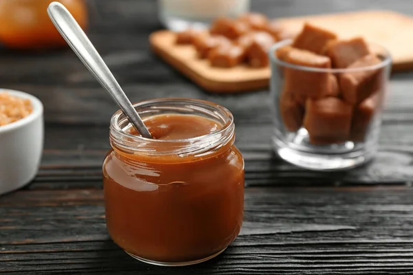 Jar with tasty caramel sauce and spoon on wooden table. Space for text Stock Photo