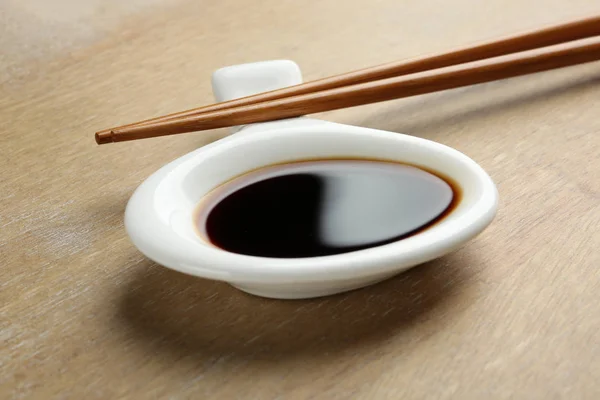 Dish of soy sauce with chopsticks on wooden background, closeup Royalty Free Stock Images