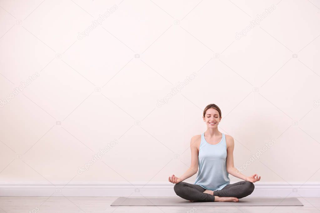 Young woman meditating near light wall, space for text. Zen concept