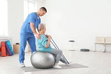 Professional physiotherapist working with elderly patient in rehabilitation center. Space for text clipart
