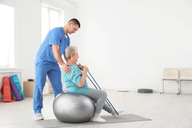 Professional physiotherapist working with elderly patient in rehabilitation center. Space for text clipart