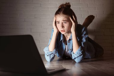 Karanlık odada yerde laptop ile şok genç kız. İnternet tehlikesi